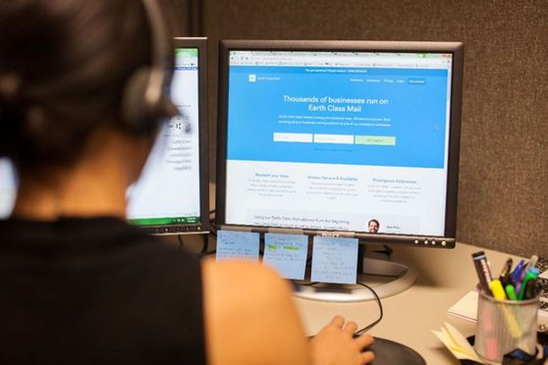 A support team member at a desk with the Earth Class Mail site on screen